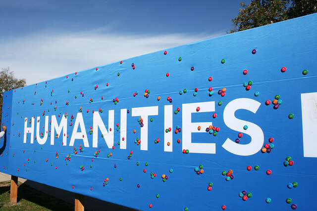 The word "humanities" in white block letters on a blue banner covered in small, brightly colored pins