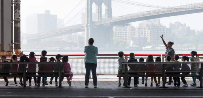 Photo of a children sitting on benches, in front of a bridge