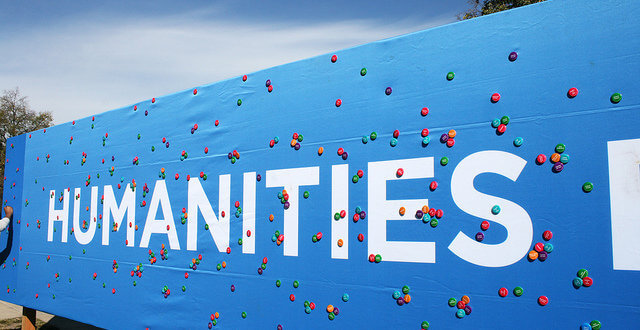 Large sign reading "HUMANITIES" in bold white text against a baby blue background, with colorful buttons placed haphazardly around the sign.