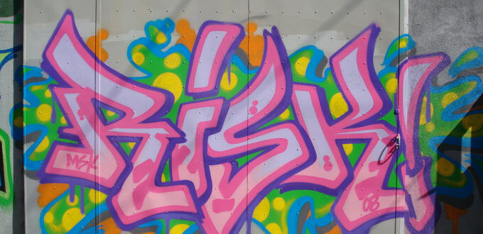 The word "RISK" in bold pink and multicolored graffiti against a concrete wall