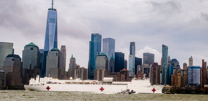 Two large white ships with red crosses on the river in front of the New York City skyline